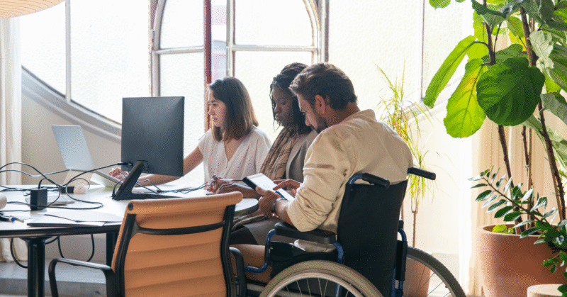 A diverse team working together in an office, including a professional using a wheelchair, represents inclusion and accessibility in the workplace.