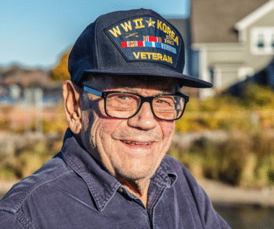 Smiling World War II veteran wearing a Navy cap standing outdoors near his home — representing veterans eligible for VA Aid and Attendance benefits.